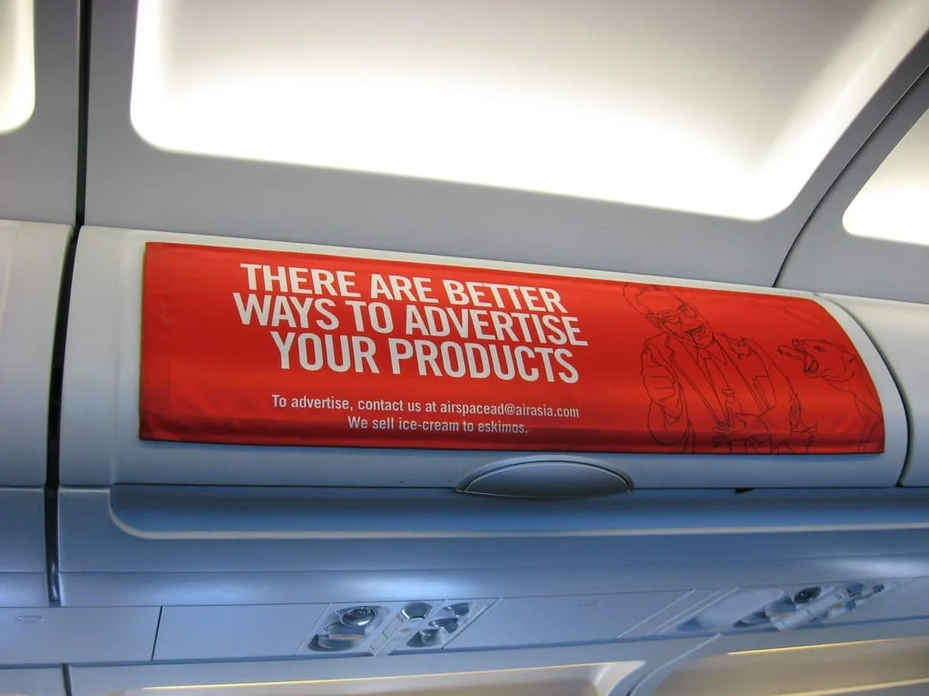 In-flight overhead advertising banner inside an airplane promoting AirAsia ad space.